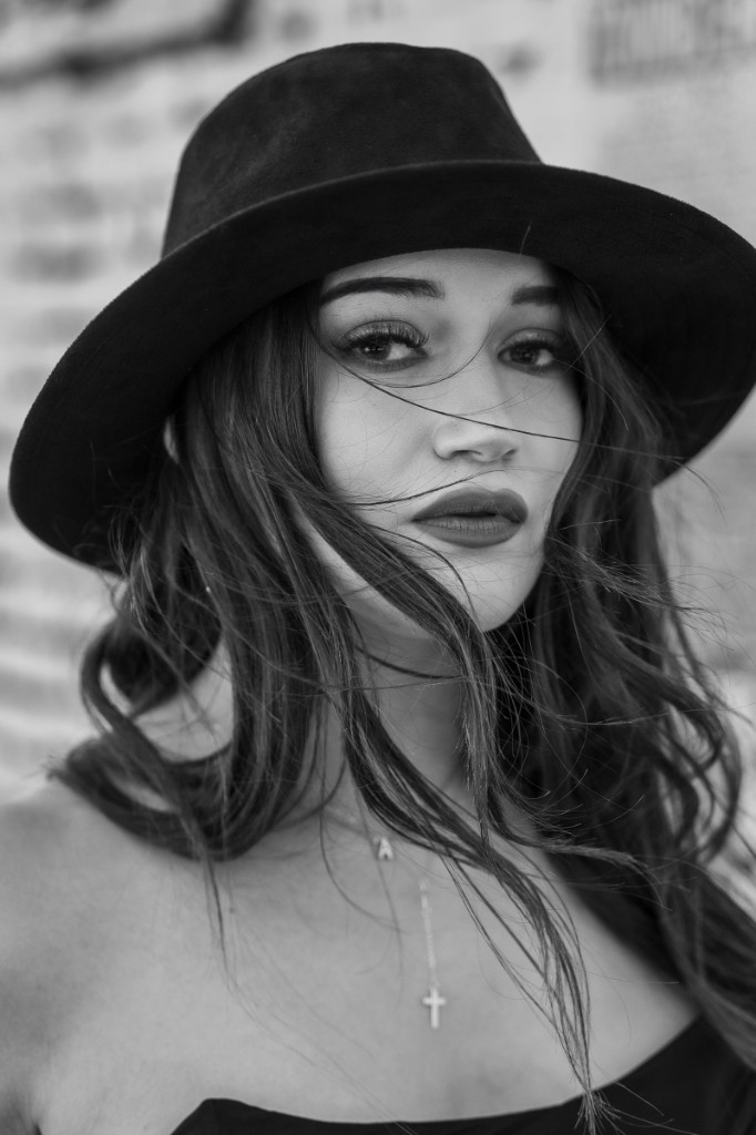 Editorial portrait in a wide-brim hat against a textured brick wall